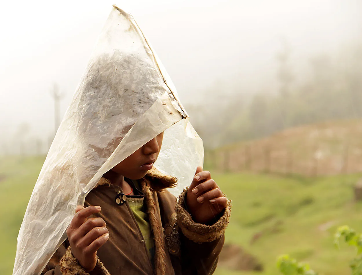 A child sheltering under a plastic sheet in the rain
