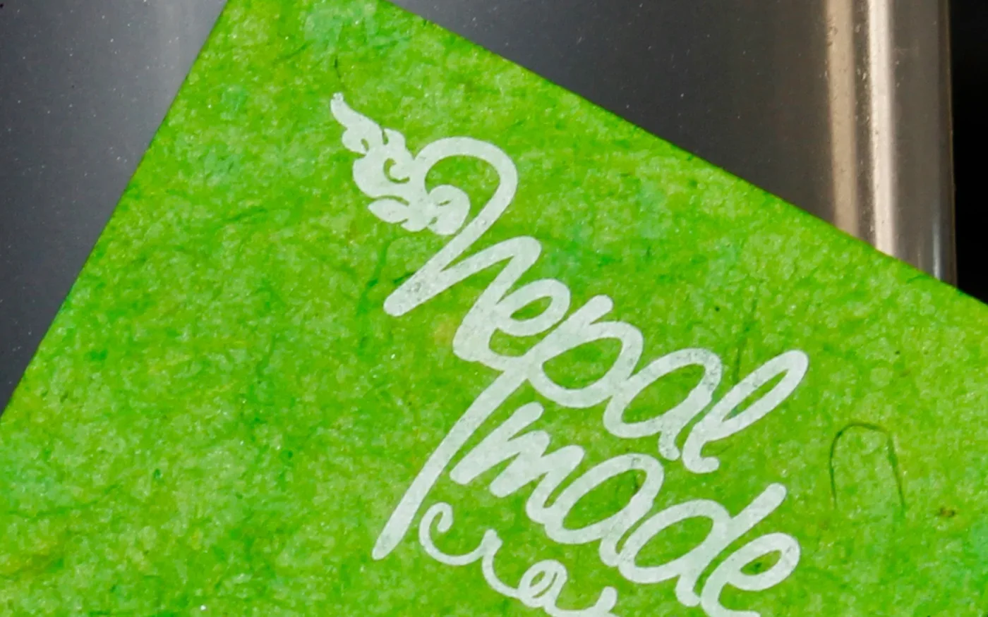 The Nepal Made Craft logo printed in white on a green business card of handmade lokta paper